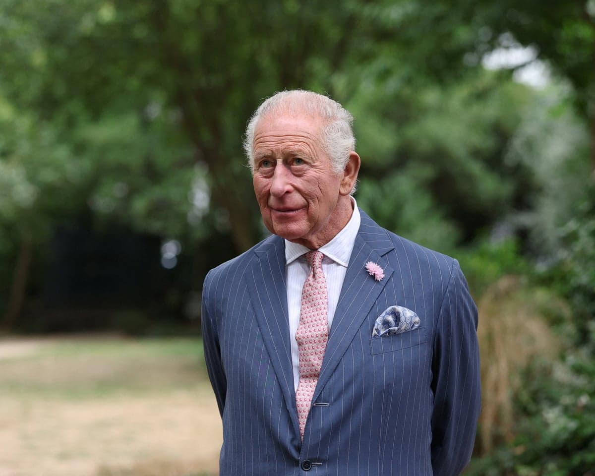 King Charles stands at a garden party in London with trees in the background