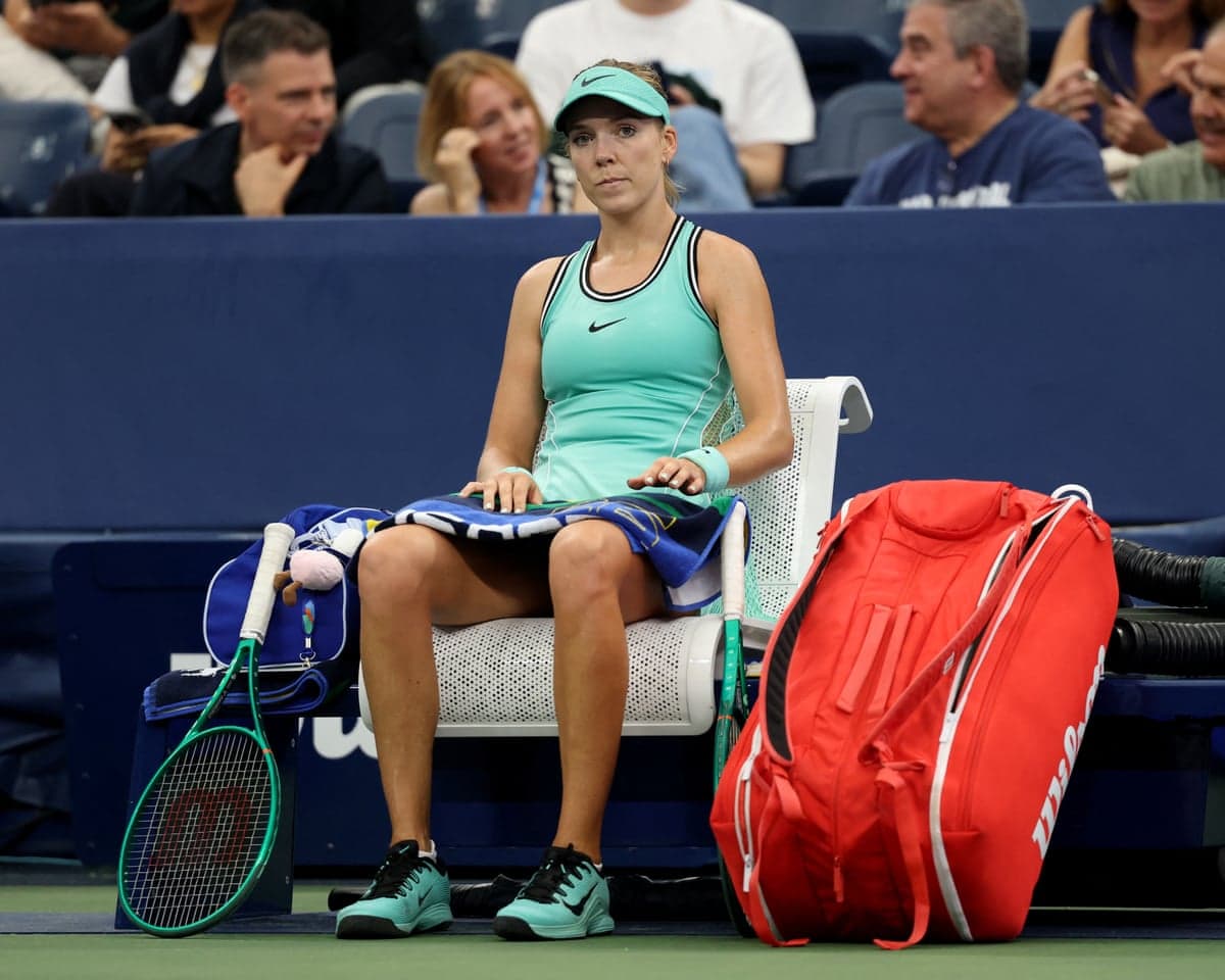 Katie Boulter sits courtside on a chair holding a towel during a break in her match