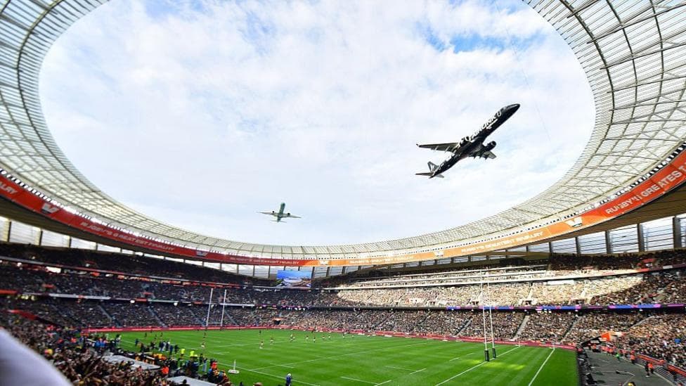A fish-eye view from the stands of a rugby stadium looking up at the sky as two planes fly in close formation above.
