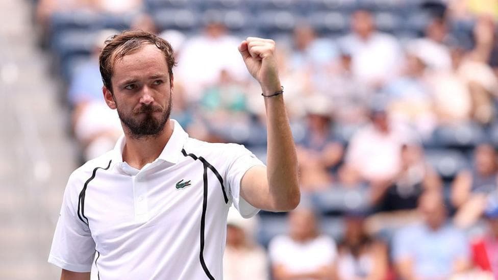 Daniil Medvedev, bearded and wearing a white polo shirt, raises his left fist in celebration