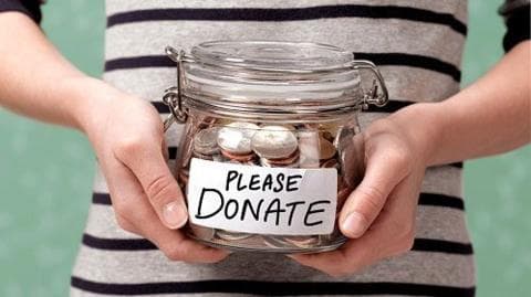 A shot of someone's torso, in a black and white striped top, holding a glass jar with coins in it. On the front is a label that reads: Please donate.
