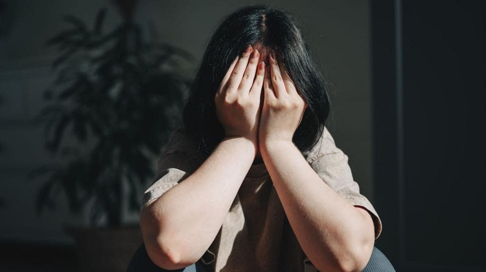 A young woman with dark hair with her head in her hands. her face is not visible, just her forearms and her hair