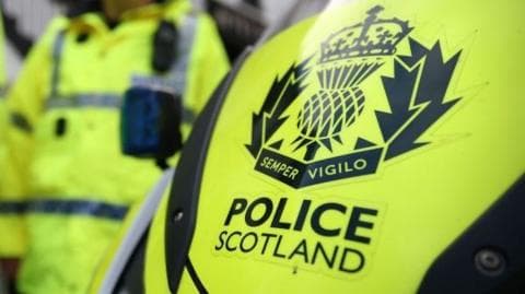 Yellow vehicle with POLICE SCOTLAND in bold letters, and officers in yellow uniforms in the background.