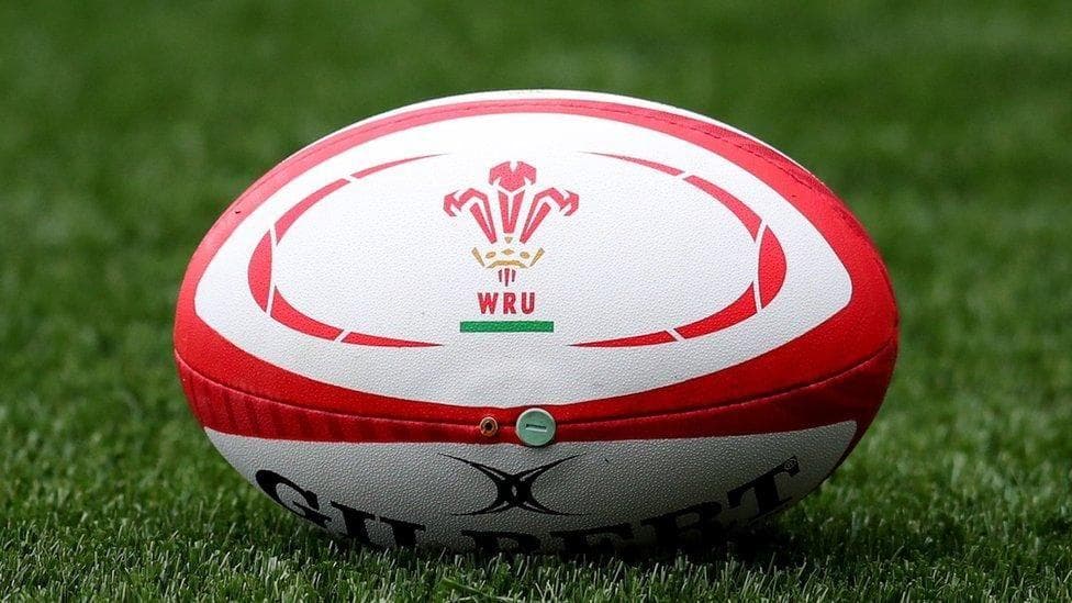 A red and white rugby ball on a grass pitch with WRU branding on it.