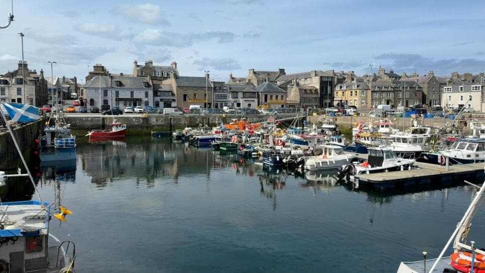 A mixture of fishing boats and pleasure boats at Fraserburgh port. There are buildings behind them