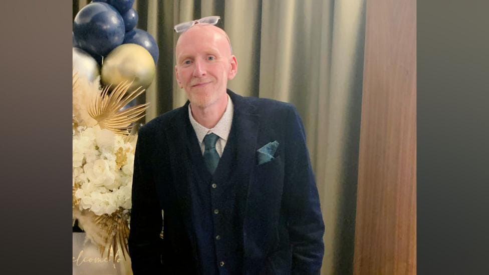 Image shows Simon Gettings, who has a bald head, glasses on top of them, and is wearing a three-piece suit.