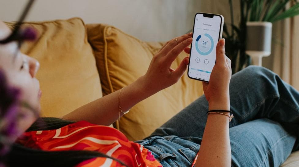 A picture of a woman in a red t shirt and jeans leaned back on a sofa checking her energy consumption on a mobile app.