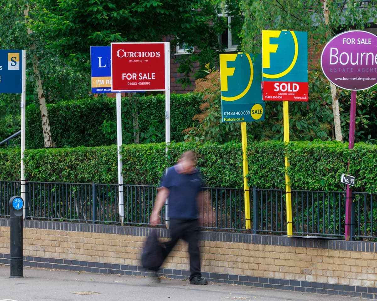 Someone walking past a row of For Sale signs on properties