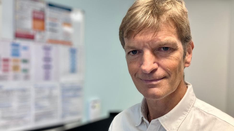 A man in a white shirt in a GP consulting room