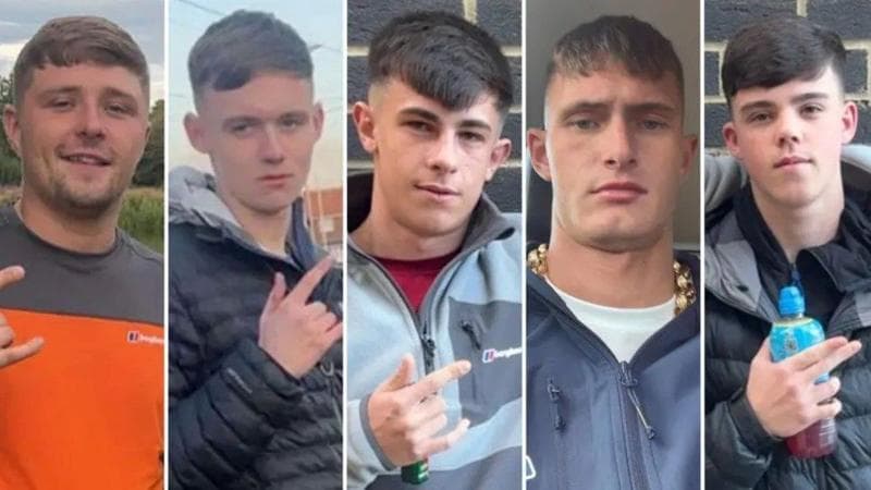 Five young men in their late teens and early 20s. They all have similar haircuts, with a fringe and faded back and sides. Four of them are gesturing with their fingers. Three of them extend their thumb, index, and pinky fingers - leaving their middle and ring finger tucked down. One points with his index and middle finger whilst holding a Lucozade bottle. They are all dressed in casual clothing.