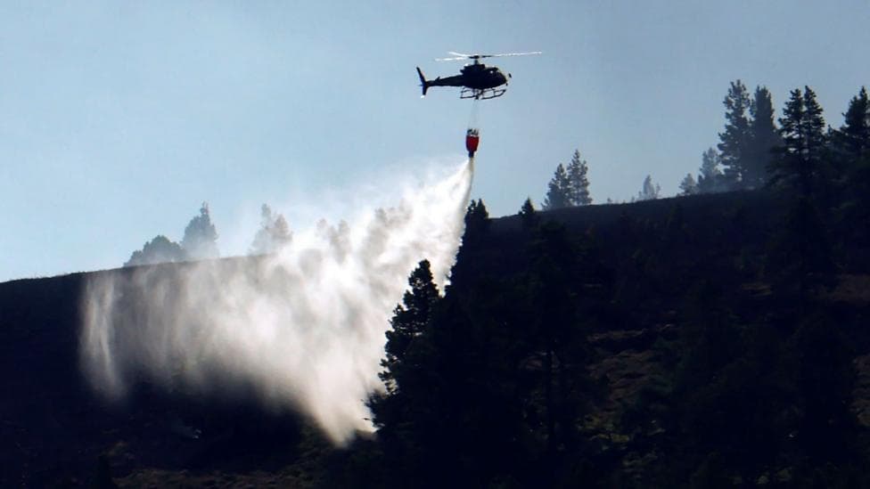A helicopter, silhouetted against smoke, drops water on an area of forestry in the Cairngorms.