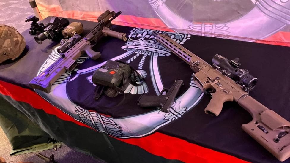 Guns laid out on a table with a military flagged drained over the top
