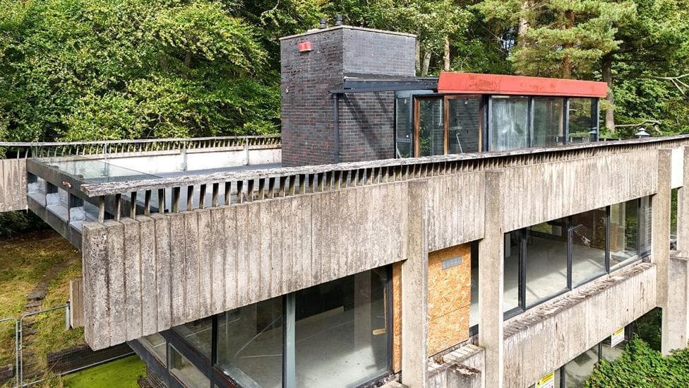 A brutalist studio in the Borders made of cement and glass which is in severe decay with windows boarded up