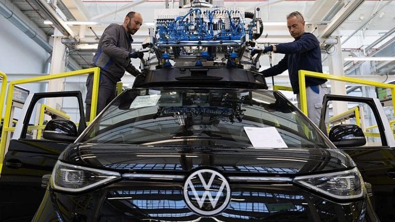 Workers install the sensors on the roof of a shiny black Volkswagen ID. Buzz electric van at the company's factory.