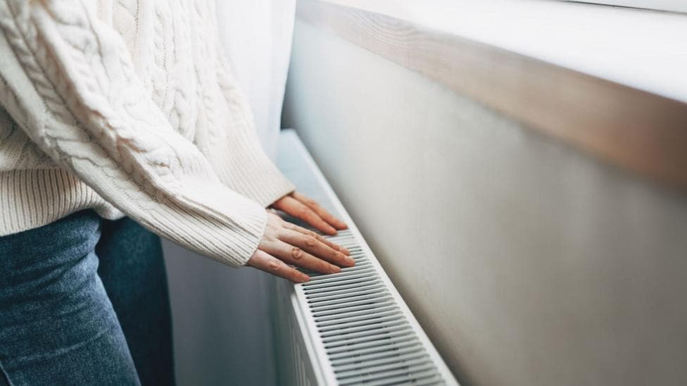 Person wearing white jumper and jeans placing their hands on a radiator.