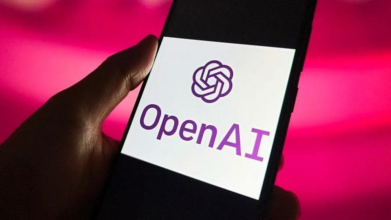 A hand holds a phone which has the OpenAI logo on its screen.