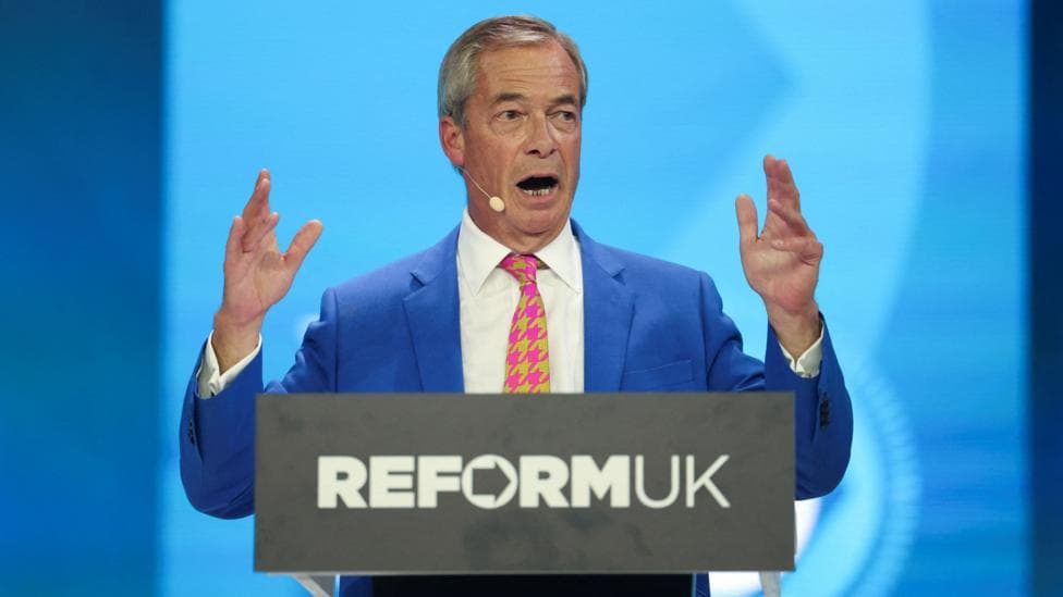 Nigel Farage holds up his hands as he gives his conference speech from behind a podium with Reform UK's logo.