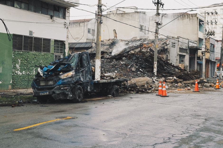 A damaged vehicle and debris on an urban street after a fire incident, depicting aftermath and destruction.