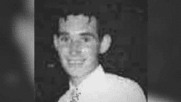A grainy black and white image of Thomas Burns, who is in a shirt and tie and smiling at the camera.