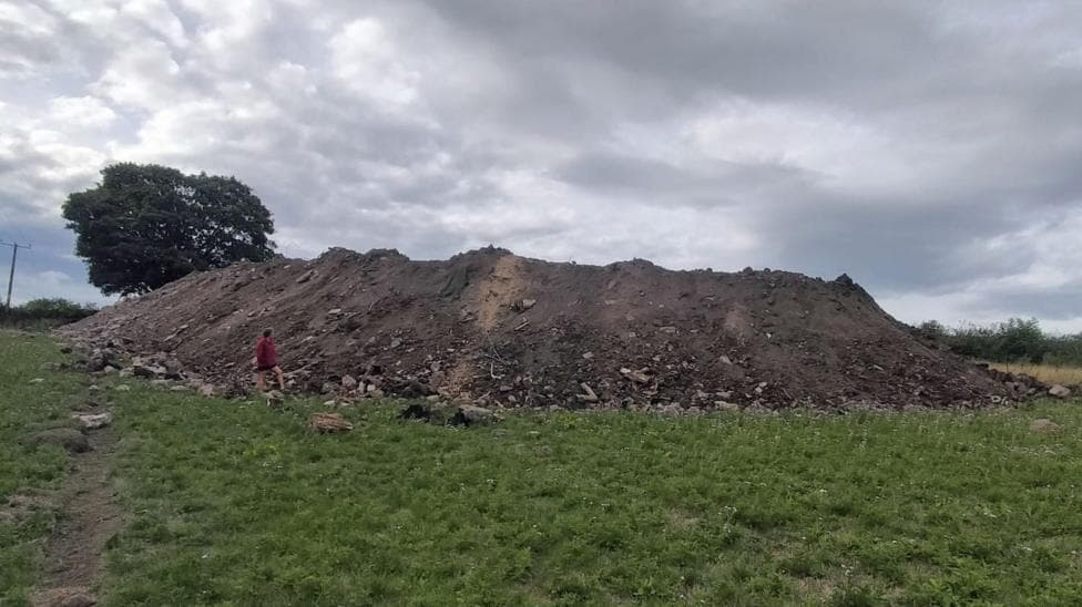 A mound of soil and earth in a field. A woman looks up at it