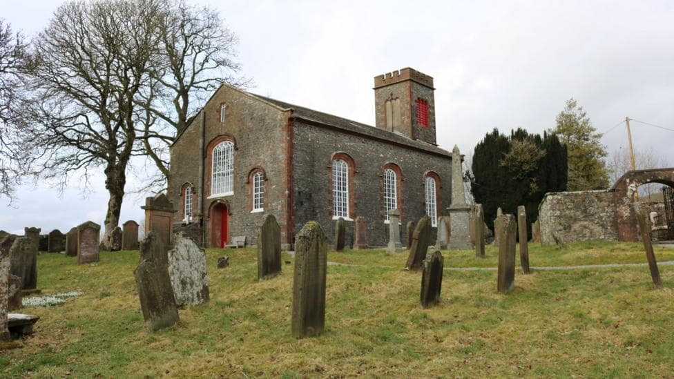 A church building in a graveyard with trees around it