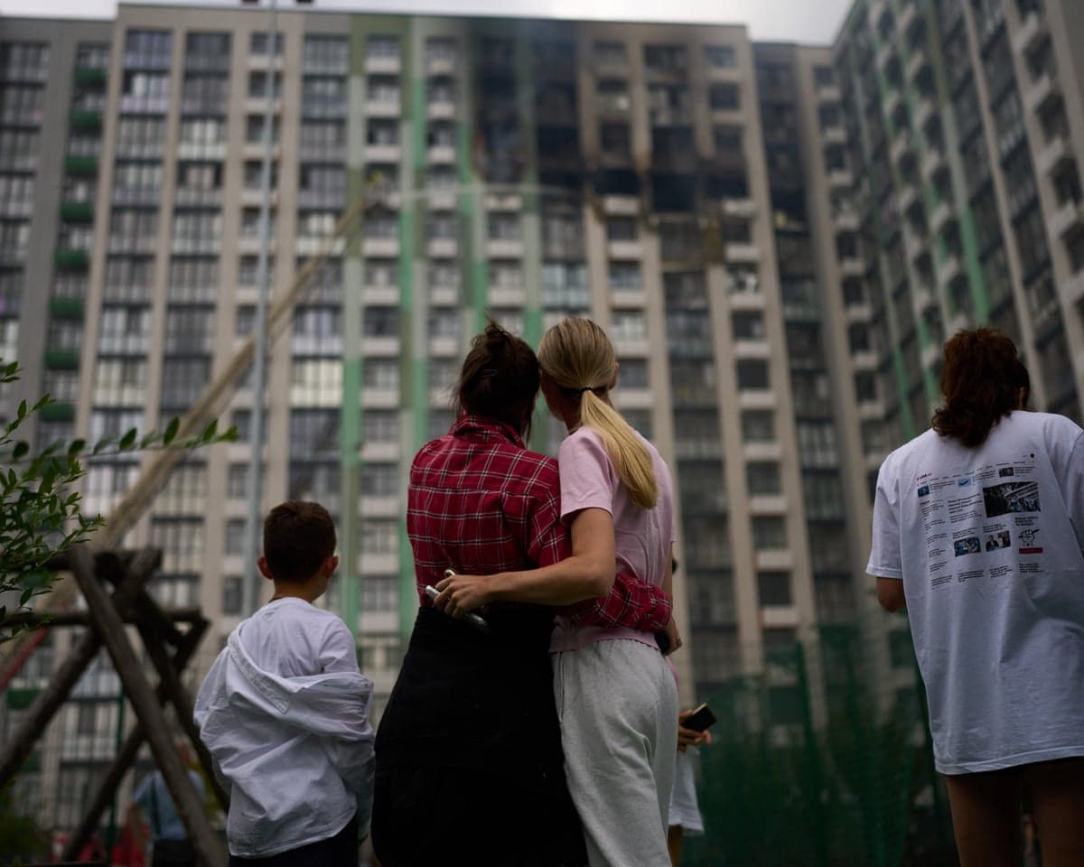 Two women hold on to one another as they watch firefighters try to extinguish a fire halfway up a residential building