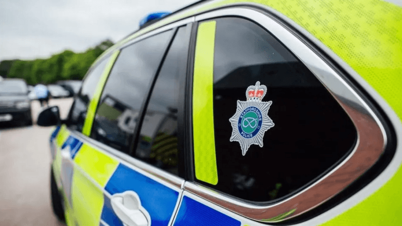 Image shows the back left hand side of a police car, with yellow and blue panels and a Staffordshire Police badge in the back window.