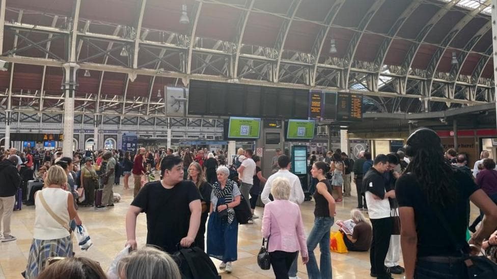 Crowds fill the concourse of London Paddington station with the departure boards blank showing no services.