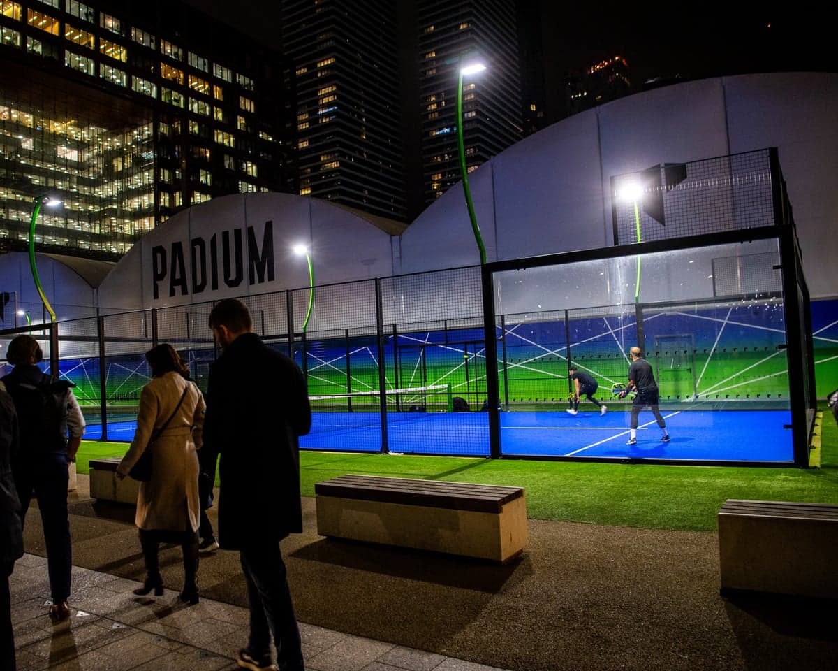 A night shot of people walking past floodlit padel courts