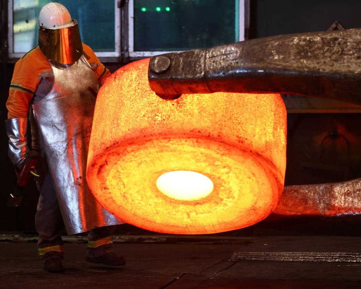 An employee works on a glowing steel element that has been heated in a classic natural gas-fired furnace at a plant in Germany