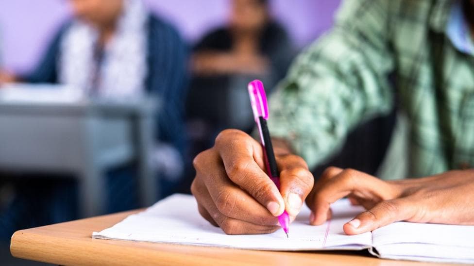 Close up shot of college student writing notes on book at classroom