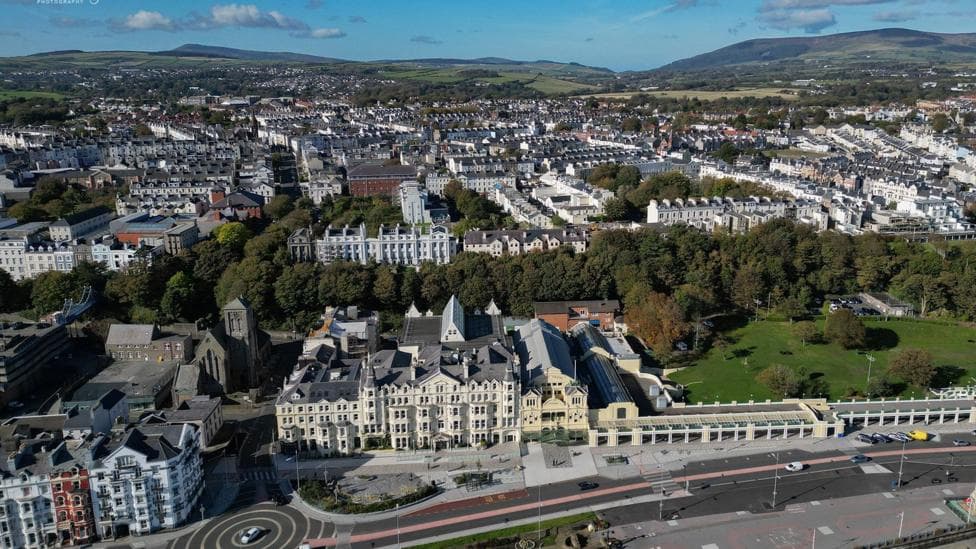An aerial view of Douglas from the promenade on a bright day, showing hundreds of buildings with areas of trees breaking it up.