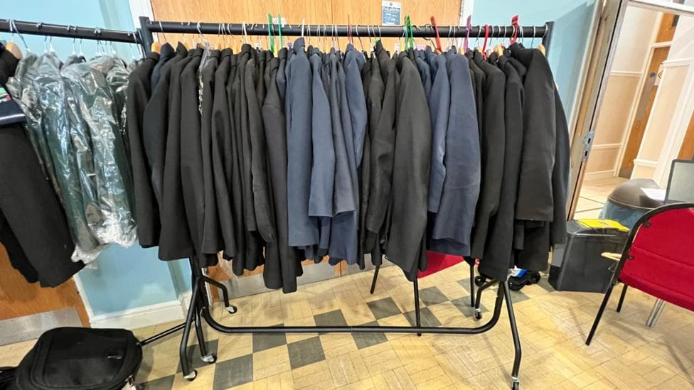 A rack of school uniform black and navy blazers. A red chair is to the left of the rack.