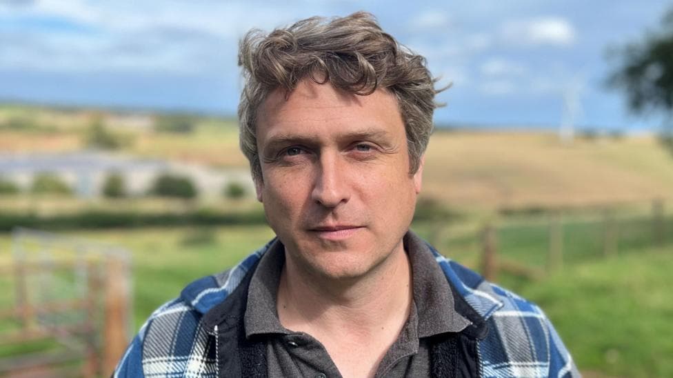 A man with long curly grey hair standing in a field.