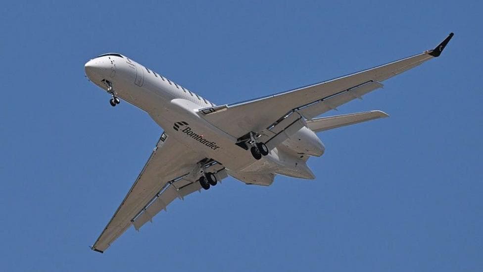 An image showing a Bombardier Global 8000 flying, with its bottom visible, showing its wheels and a Bombardier logo.