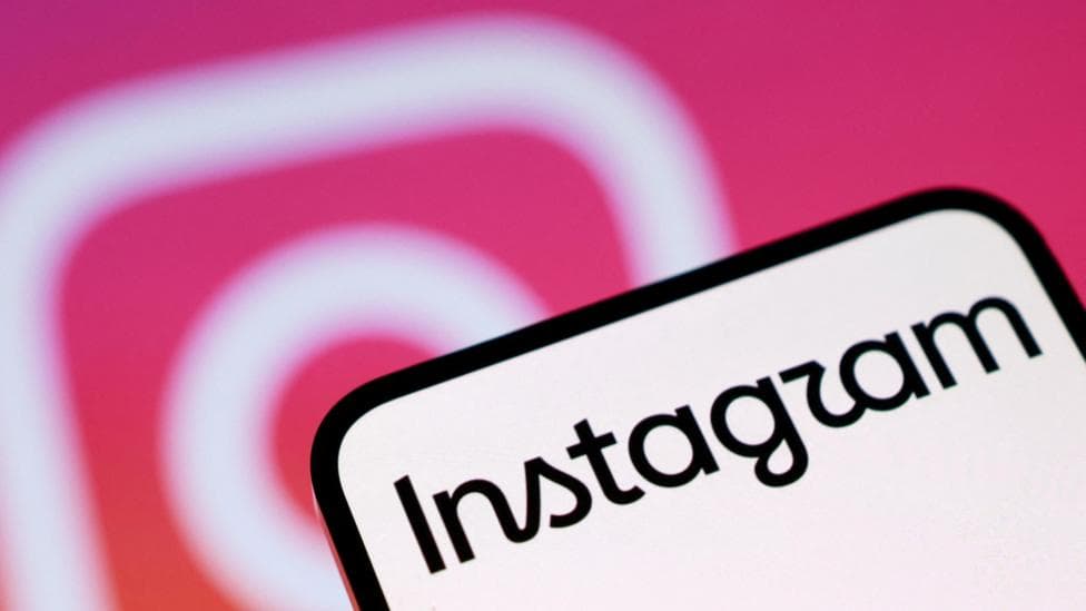 A phone screen with Instagram written on it. In the background is the pink and white Instagram camera logo