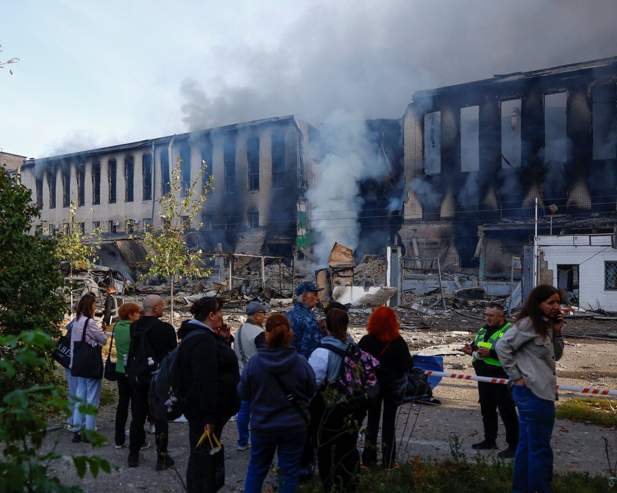 People gather behind a barrier looking at a smoking building damaged by a missile strike
