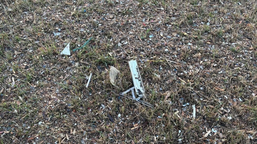 Small scraps of metal and plastic pictured between grass blades close up.