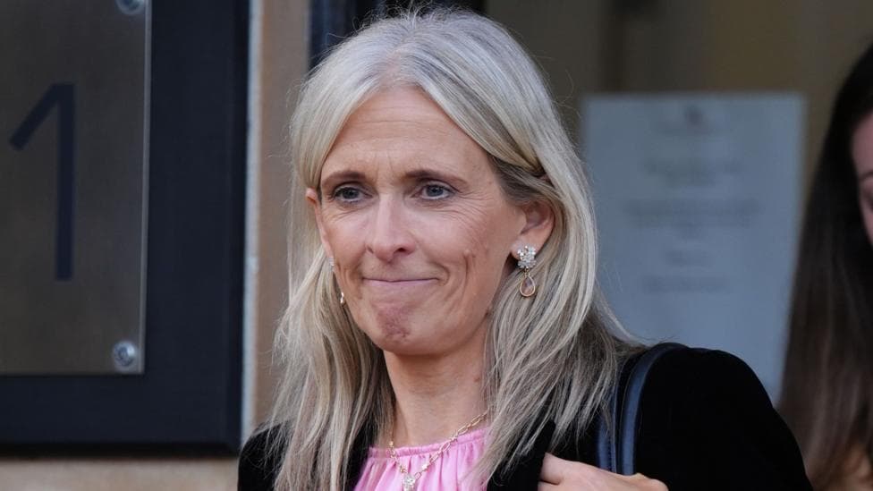 Ruth Charteris has long, white blonde hair and is walking outside a court building. She is wearing a pink top and black blazer with a gold necklace and earrings