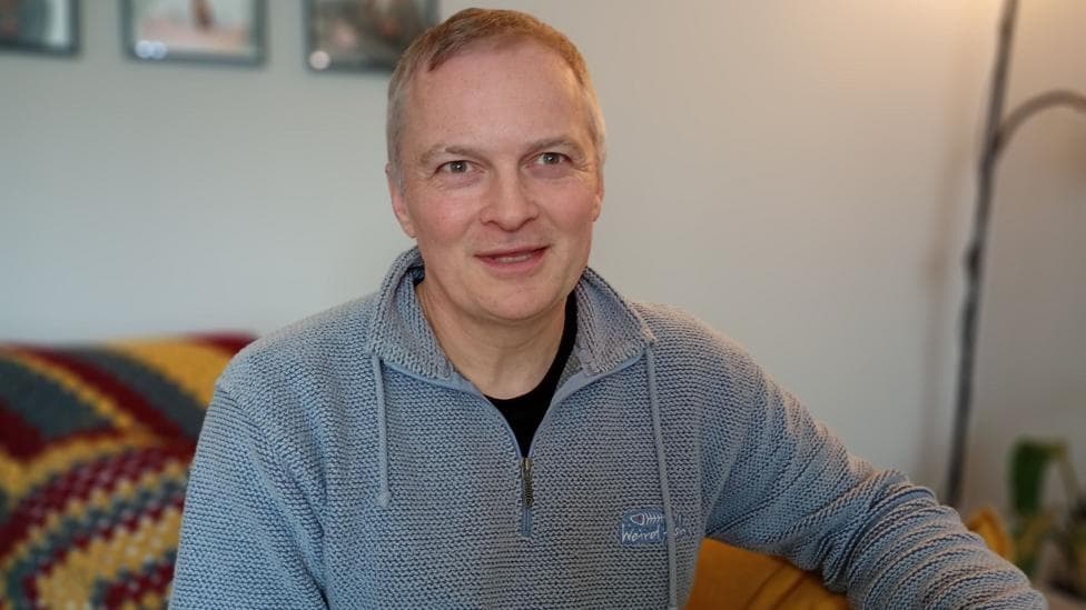 A man with grey hair wearing a grey 1/4 zip