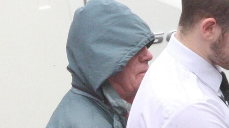 Alan MacPherson is wearing a blue waterproof jacket with the hood up as he is led away by a custody officer