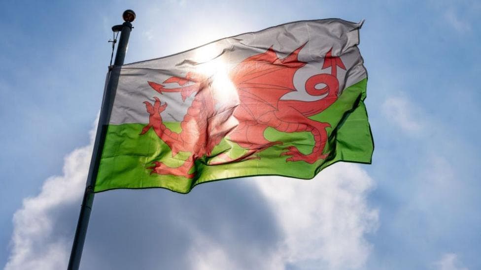 A Welsh flag flying in the wind, made up of a red dragon on a green and white background.