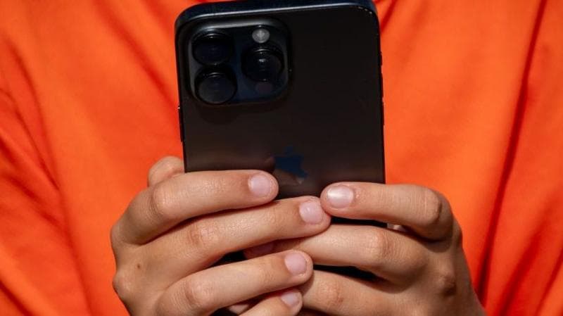 Close-up of a child's hands clasped around a black smartphone