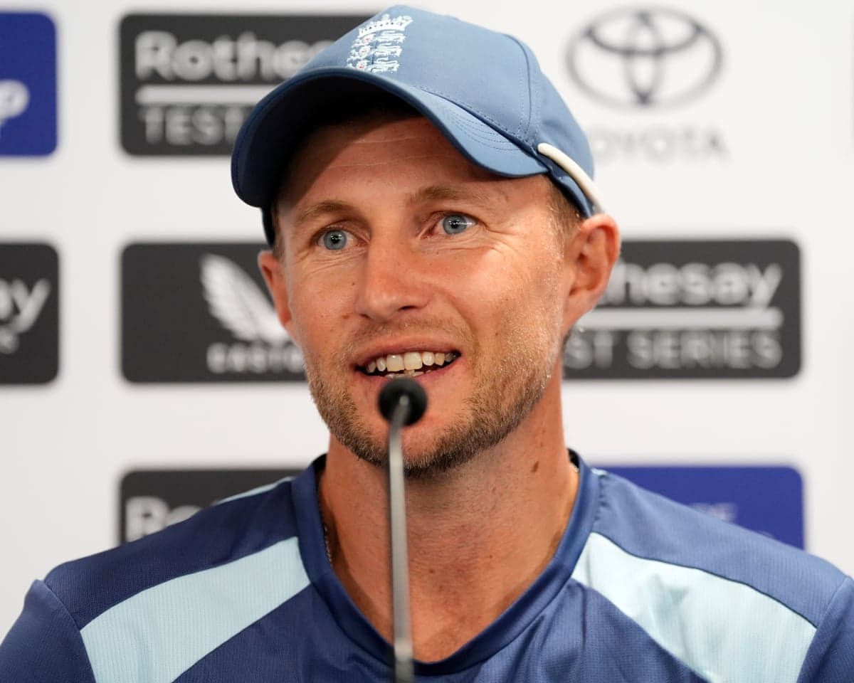 Joe Root in blue England training top and baseball cap speaks at a press conference