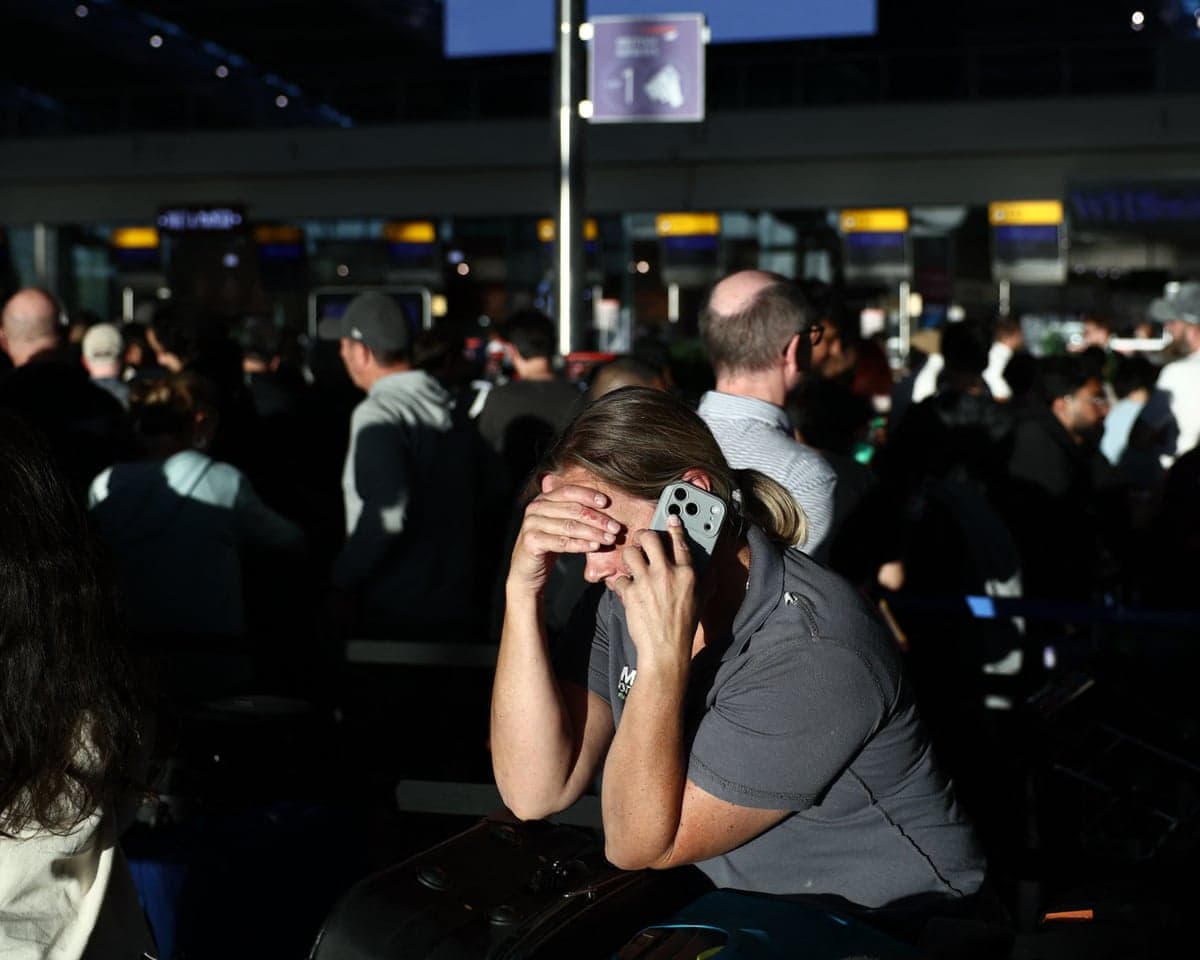 A woman hold her hand to her forehead as she talks on her mobile phone with a crowd of passengers behind her
