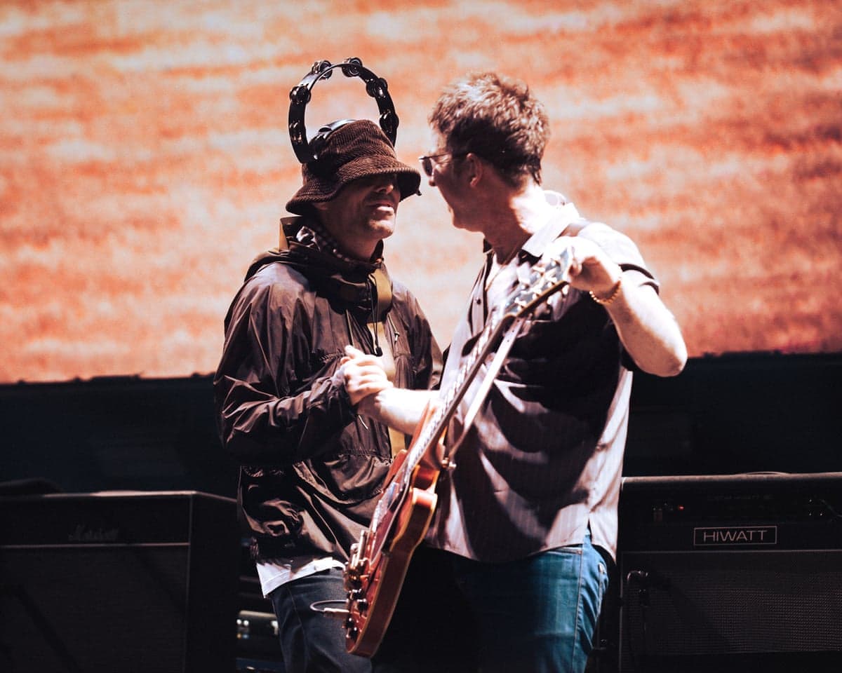 Liam and Noel Gallagher on stage, clasping hands, in Oasis: Don’t Look Back in Anger.