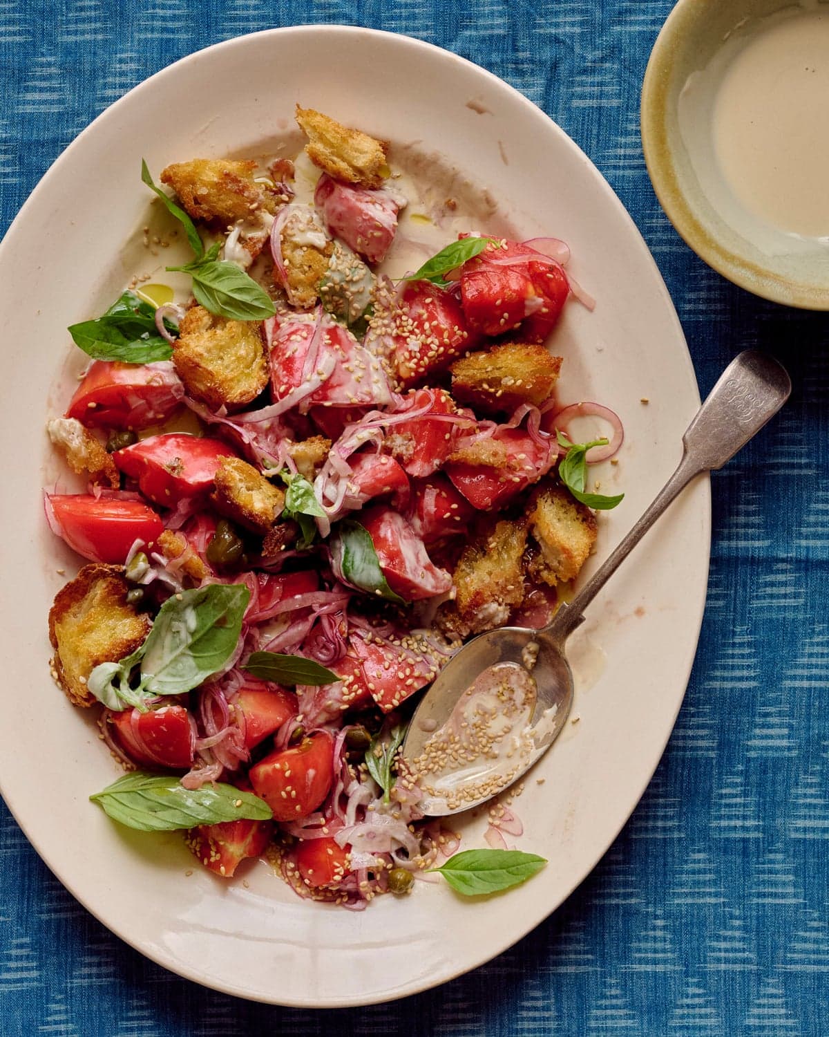 Alexina Anatole's tahini panzanella on a plate with a bowl of dressing beside it