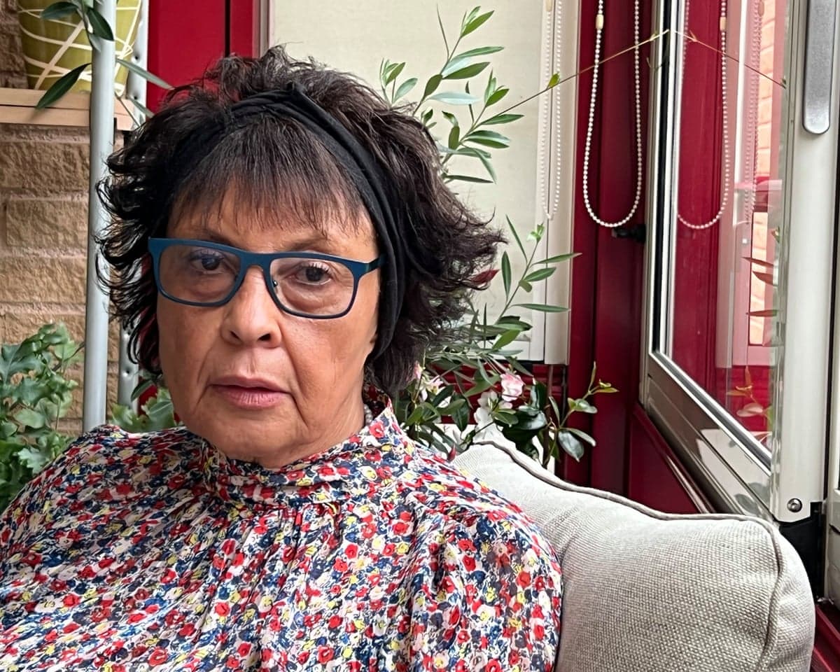 Joyce Thomas, 78, wearing blue-rimmed glasses and a flowery dress