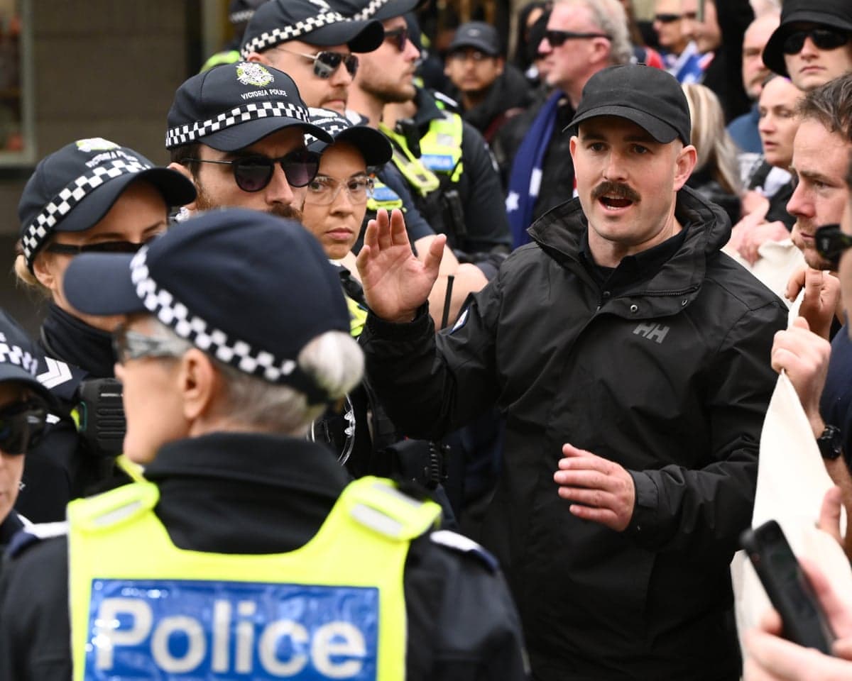 Activist Thomas Sewell raises his hand while speaking, surrounded by police and a crowd