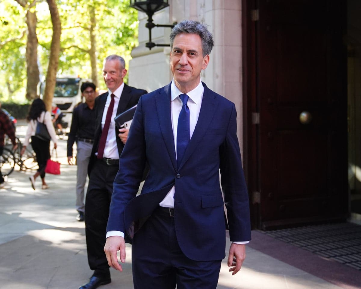 Foreign Secretary Ed Miliband smiles while walking outside, with two men behind him